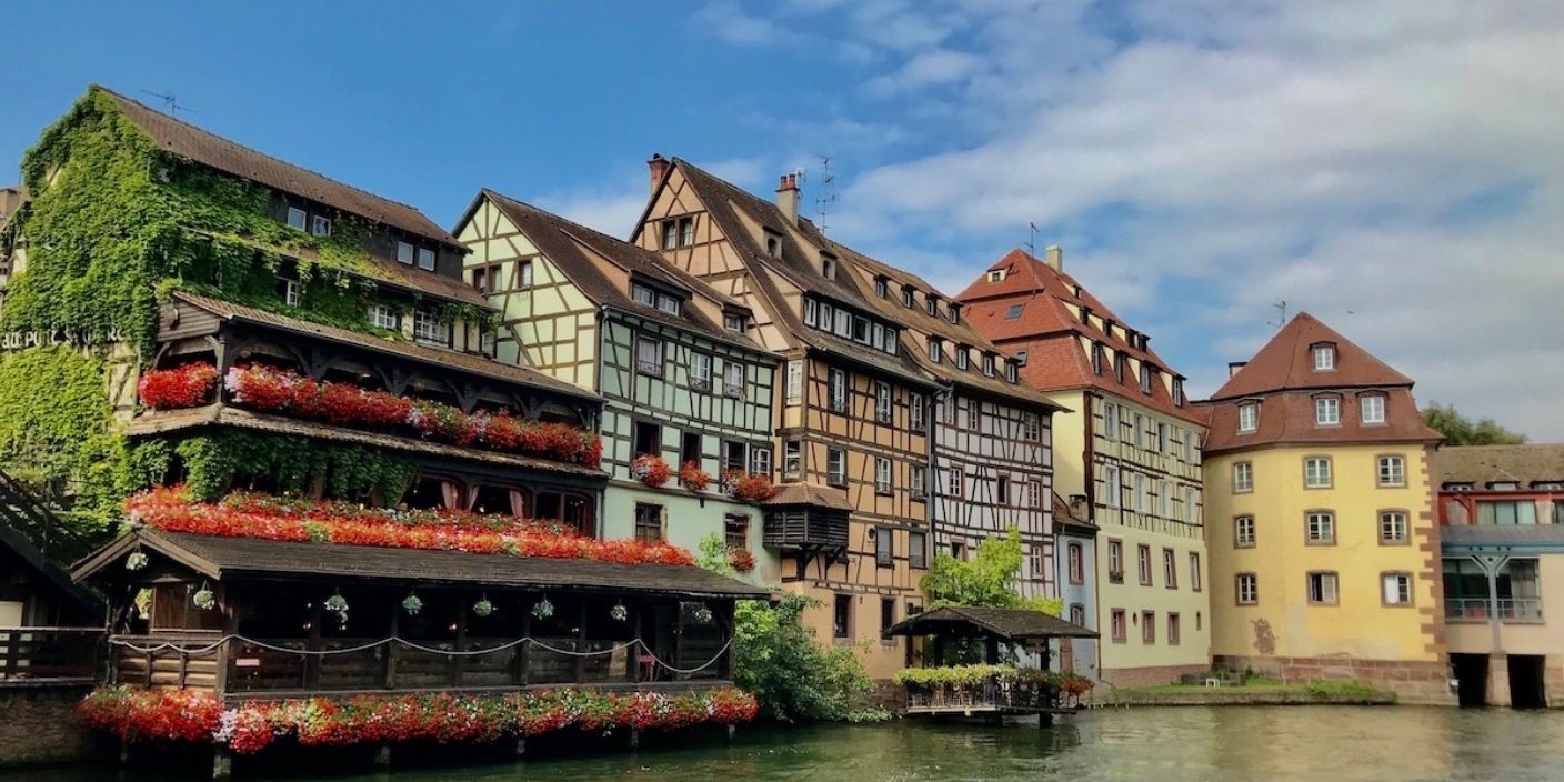 Maisons traditionnelles à colombages dans le quartier de la Petite France à Strasbourg, avec des balcons fleuris et une rivière en premier plan.