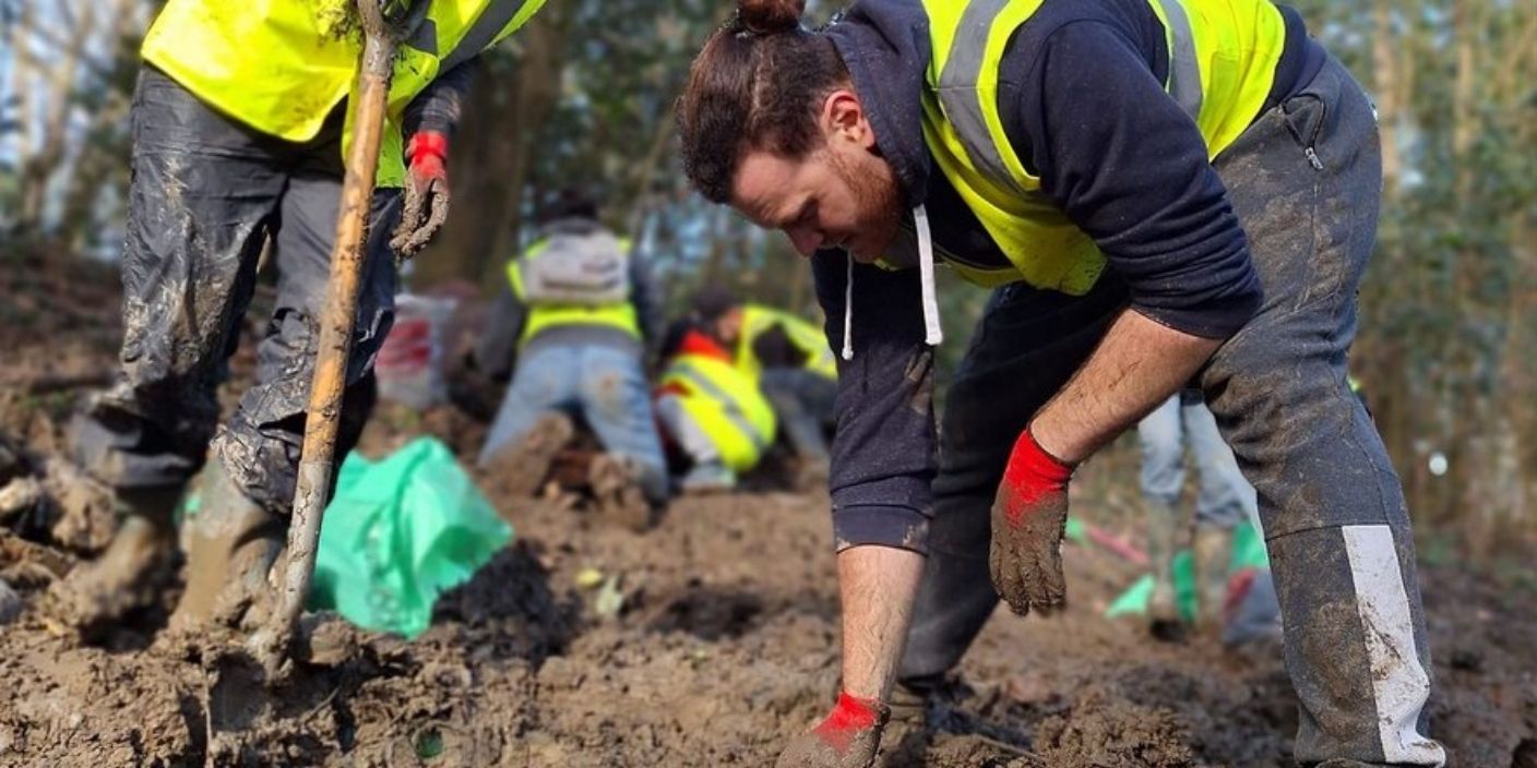 Bénévoles en gilets jaunes participant à une action de reforestation dans la boue, illustrant un team building RSE axé sur la plantation d’arbres à Toulouse.